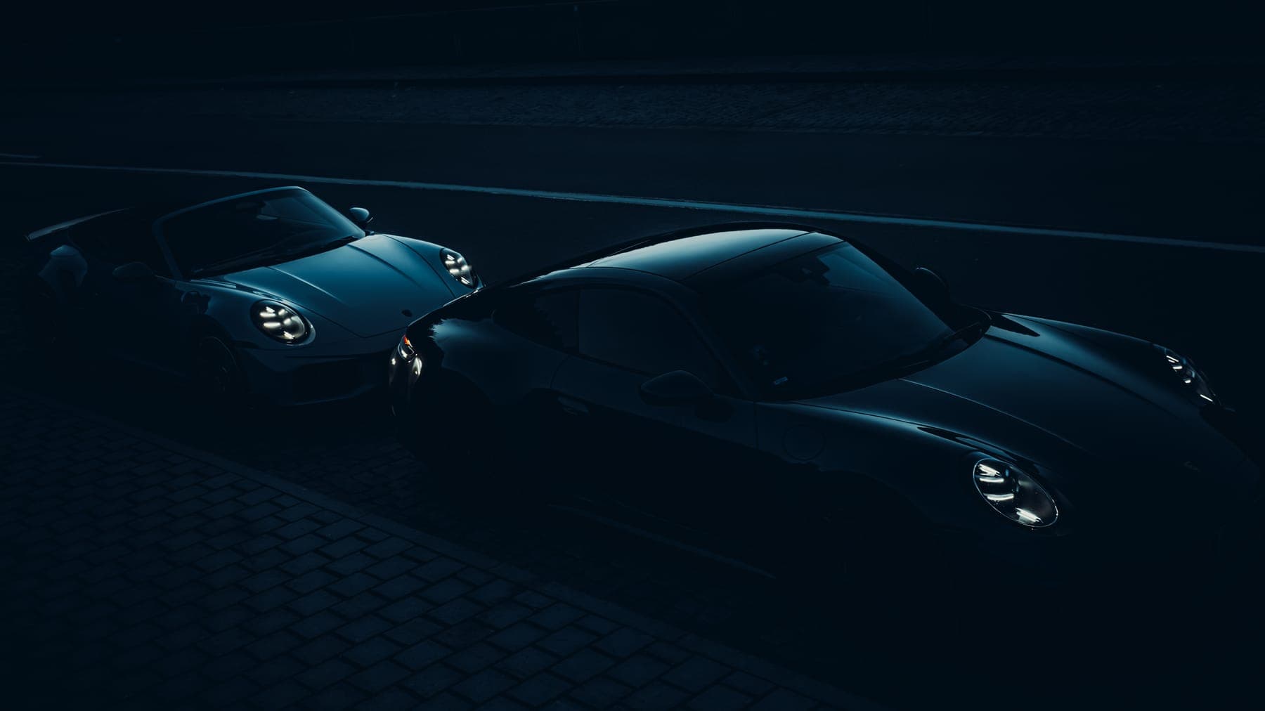 Zwei Porsche 911 bei Nacht auf Kopfsteinpflaster.