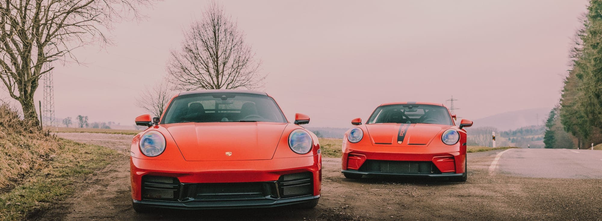 Roter Porsche 911 Turbo S und Porsche 911 GT3 frontal auf einer Landstraße.