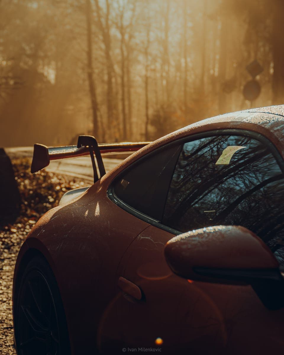 Regennasser Heckflügel eines roten Porsche 911 GT3 im goldenen Herbstlicht.