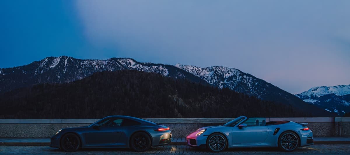 Zwei Porsche 911 Turbo zur blauen Stunde vor verschneiten Alpengipfeln.